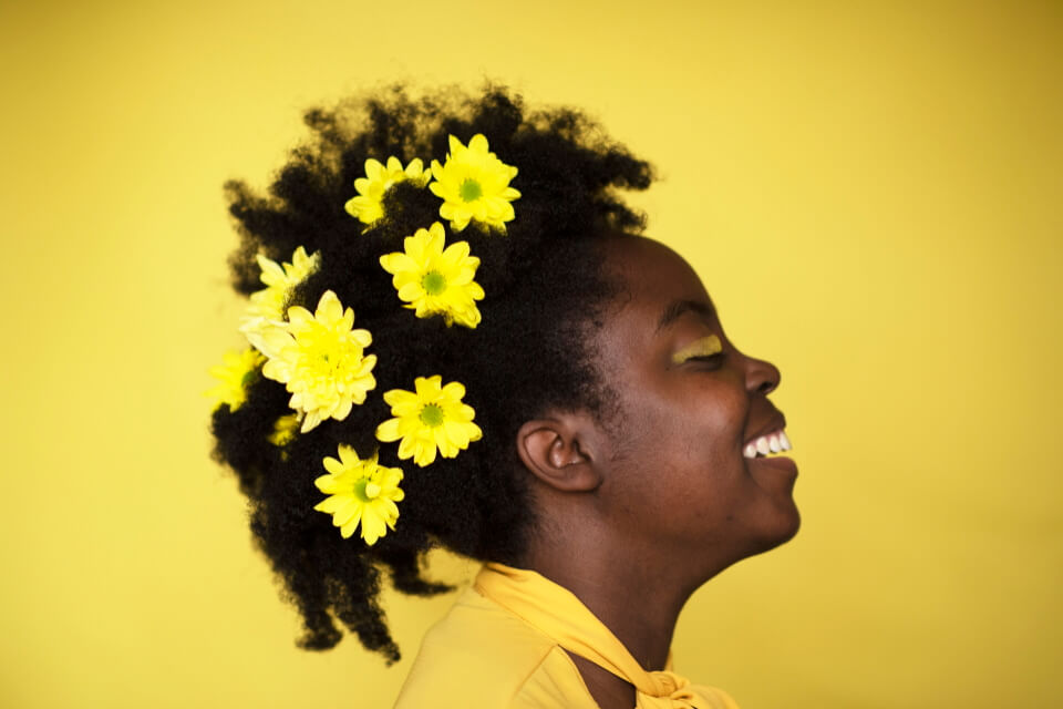Image of black woman smiling with flowers in her hair on a yellow background